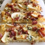 Close-up of a slice of 10-ingredient pizza topped with crispy bacon, thin pear slices, and blue cheese.