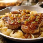 Close-up of 10-ingredient pork chops recipe, served over caramelized onions and topped with a glossy sauce and chives.