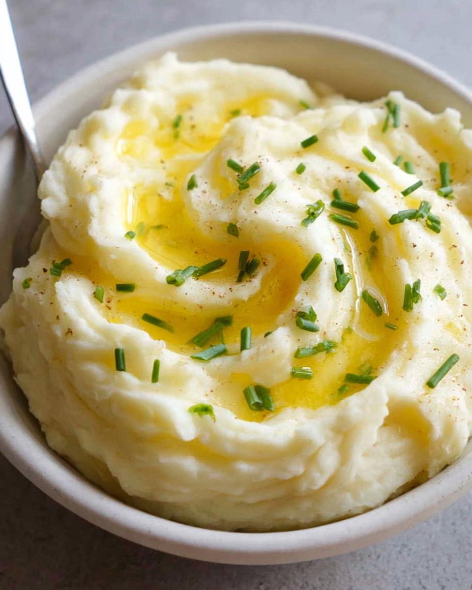 A bowl of creamy 12-Ingredient Mashed Potatoes topped with melted butter and fresh chives.