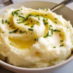 A bowl of fluffy 12-Ingredient Mashed Potatoes topped with melted butter and fresh chives.