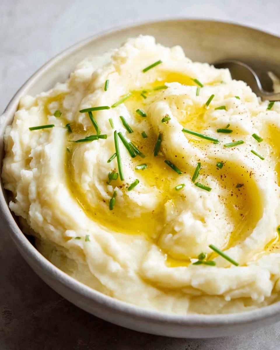 Close-up of creamy 12-ingredient mashed potatoes topped with melted butter and fresh chives.