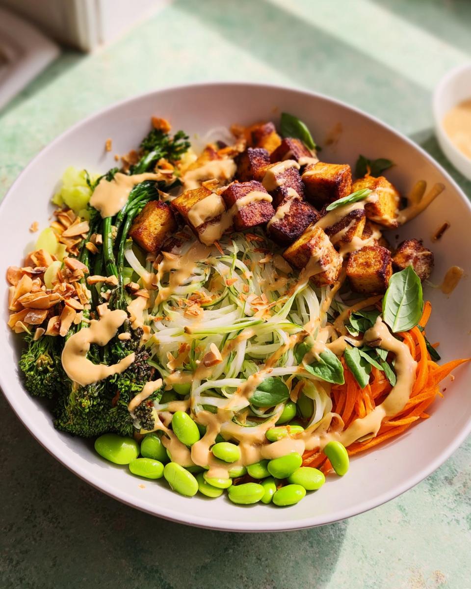 A vibrant bowl of 20-Ingredient Rice Bowls Recipe with crispy tofu, edamame, broccoli, shredded carrots, and a creamy dressing.