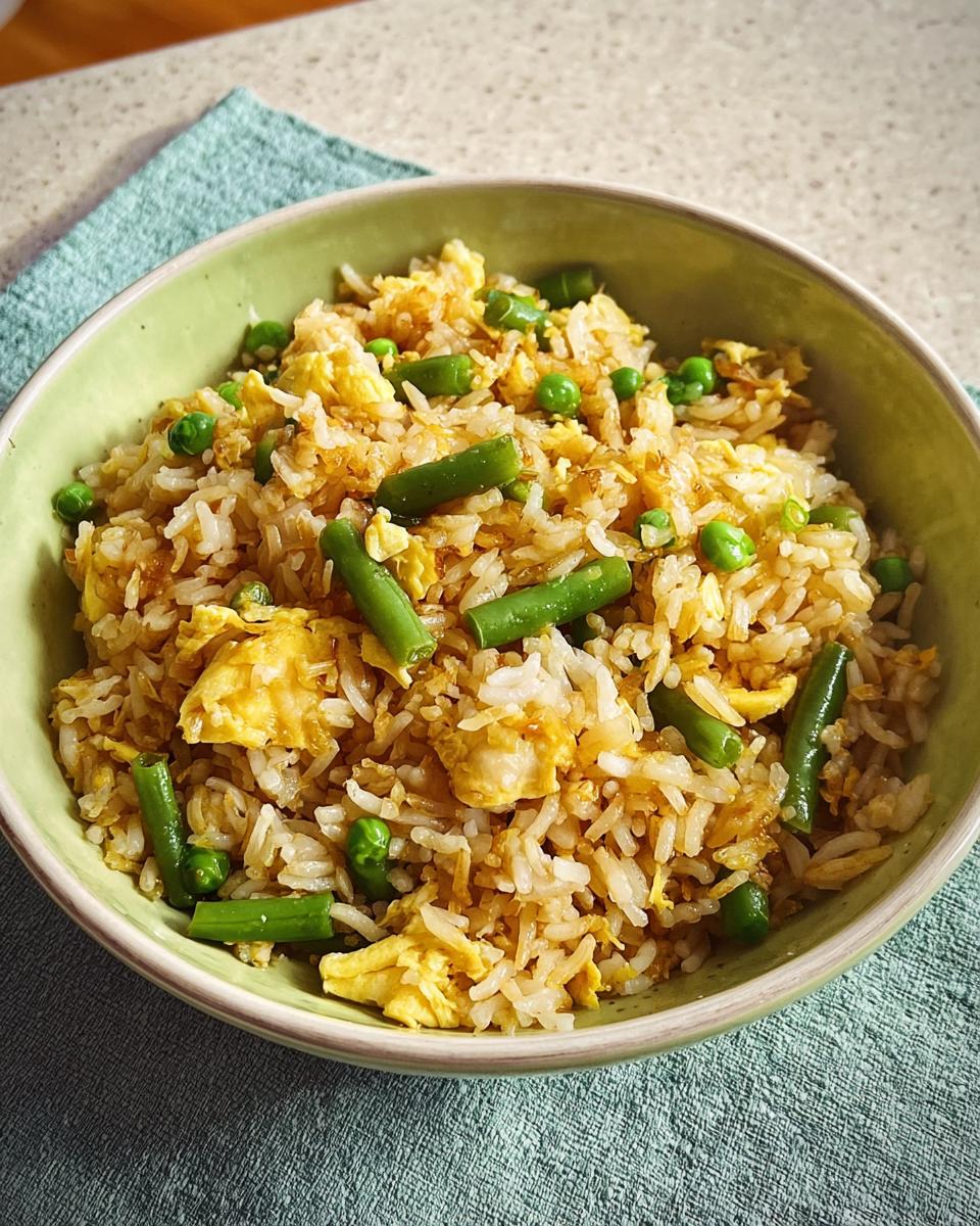 A bowl of 7-ingredient egg fried rice with scrambled eggs, green beans, and peas.