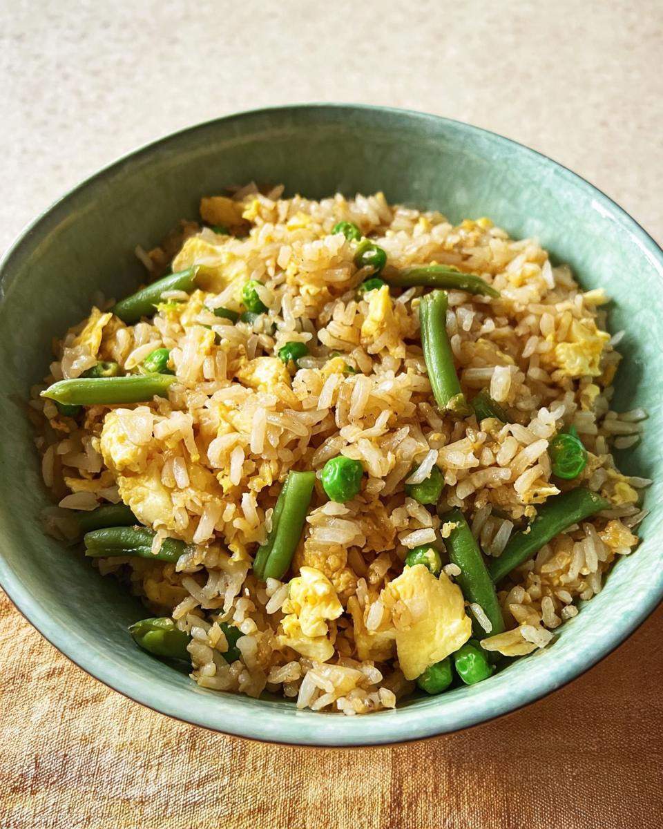 A close-up of a bowl of 7-ingredient egg fried rice with scrambled eggs, green beans, and peas.