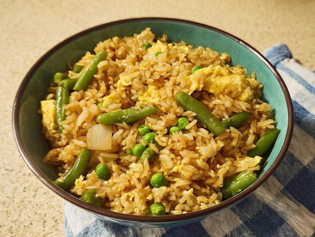 A close-up of a teal bowl filled with 7-ingredient egg fried rice, featuring green beans, peas, and scrambled egg.