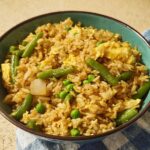 A close-up of a teal bowl filled with 7-ingredient egg fried rice, featuring green beans, peas, and scrambled egg.
