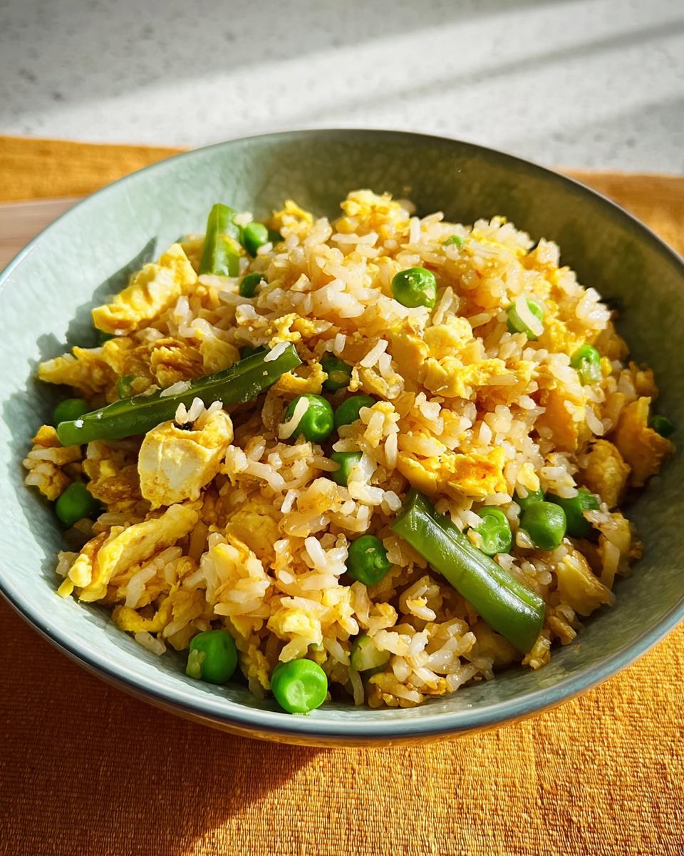 A bowl of 7-ingredient egg fried rice with scrambled eggs, peas, and green beans.