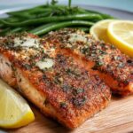 Two perfectly baked salmon fillets seasoned with herbs and garlic, served with lemon slices and green beans.
