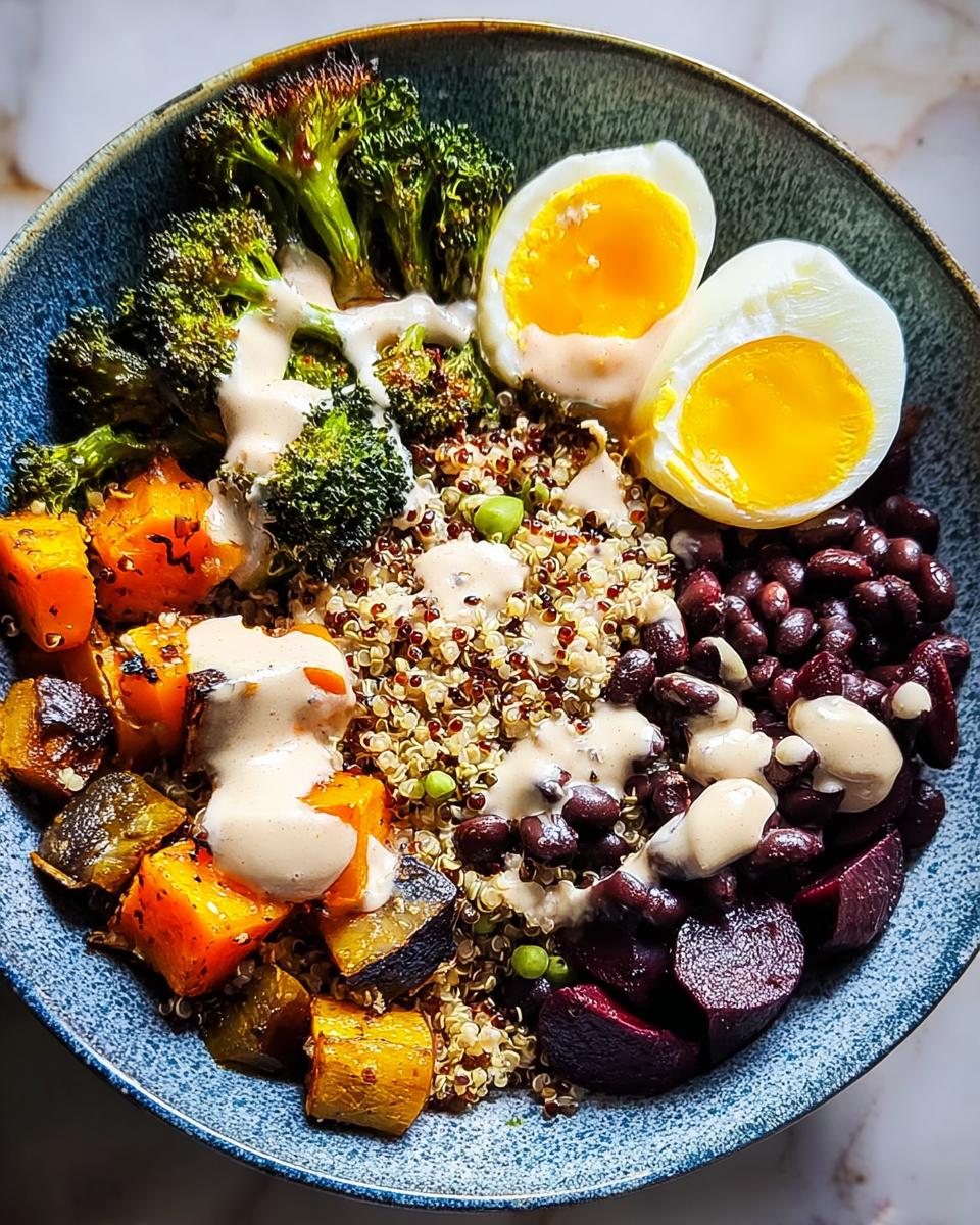 A colorful and healthy breakfast bowl featuring quinoa, black beans, roasted vegetables, and a soft-boiled egg, drizzled with dressing.