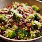 A vibrant bowl of broccoli couscous salad, featuring tender broccoli florets, pearl couscous, dried cranberries, crispy bacon bits, and grated Parmesan cheese.