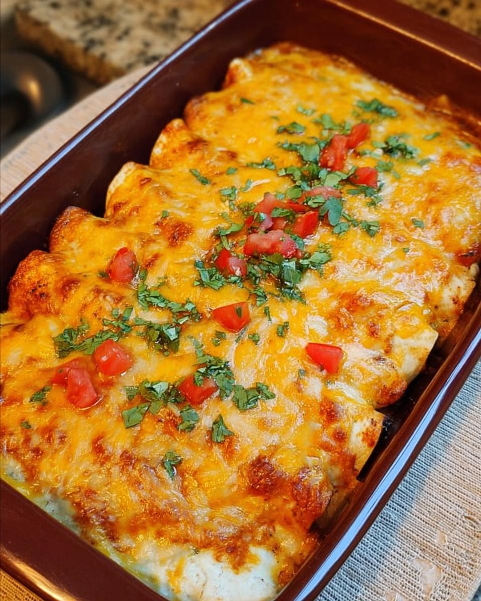 Close-up of baked chicken enchiladas topped with melted cheddar cheese and fresh cilantro and diced tomatoes.
