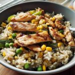 A close-up of a chicken rice bowls recipe with grilled chicken, corn, peas, and rice.
