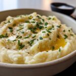 A close-up of creamy mashed potatoes topped with melted butter, fresh chives, and black pepper.