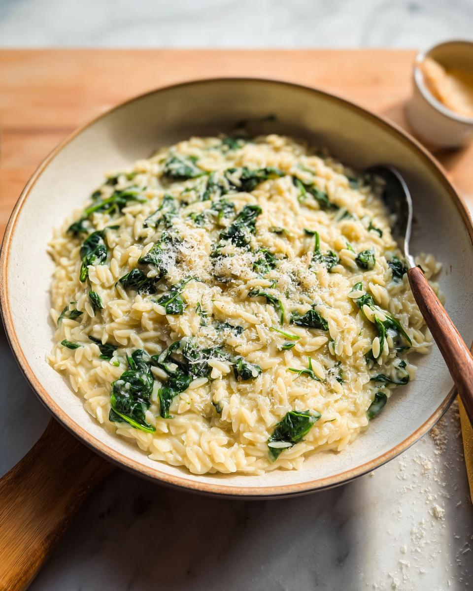 A close-up of creamy orzo pasta mixed with wilted spinach and topped with grated Parmesan cheese. A perfect veggie sides recipe.