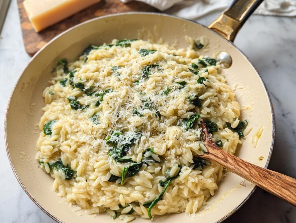 Close-up of creamy spinach orzo in a pan, topped with grated Parmesan cheese. A perfect veggie sides recipe.