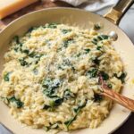 Close-up of creamy spinach orzo in a pan, topped with grated Parmesan cheese. A perfect veggie sides recipe.