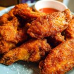 A plate of delicious, crispy baked chicken wings seasoned with spices, served with a side of dipping sauce.