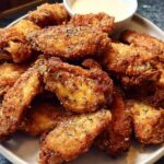 A plate full of golden-brown, crispy chicken wings seasoned with herbs, ready to be enjoyed with a side of dipping sauce.