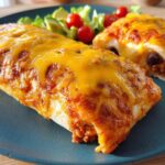 Two cheesy baked burritos filled with meat and beans, served with a side of lettuce, avocado, and cherry tomatoes. An easy dinner recipe.