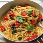 A close-up of linguine pasta with cherry tomatoes, basil, and chili flakes in a pan, perfect for easy dinner recipes meal prep.