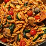 A close-up shot of fusilli pasta with cherry tomatoes, zucchini, mushrooms, and spinach in a tomato sauce, perfect for easy dinner recipes.
