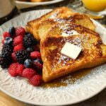 Golden brown French toast slices topped with butter and powdered sugar, served with fresh berries. A quick breakfast idea.