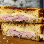 Close-up of a perfectly grilled ham and cheese sandwich, showcasing melted cheese and toasted bread.