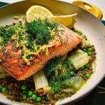 A close-up of a perfectly cooked salmon fillet served over a bed of lentils, peas, and fennel, garnished with dill and lemon zest.