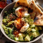 A healthy meal recipe featuring poached eggs with runny yolks, avocado, greens, and flatbread, drizzled with chili oil.