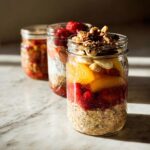 Three jars filled with layered healthy meals recipes: overnight oats, fruit, and nuts.