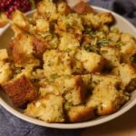 A close-up of a bowl filled with golden-brown homemade stuffing, featuring cubed bread, herbs, and aromatics.