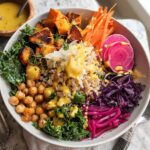 A vibrant and healthy rice bowl recipe featuring roasted sweet potatoes, chickpeas, kale, shredded carrots, red cabbage, and pickled onions, drizzled with dressing.