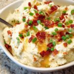 Close-up of creamy mashed potatoes topped with crispy bacon bits and fresh green onions.