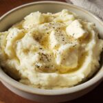 A close-up of creamy mashed potatoes topped with melting butter and black pepper, part of The Only Mashed Potatoes Recipes Recipe.