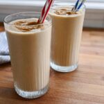 Two tall glasses filled with creamy peanut butter smoothies, topped with a swirl of peanut butter and striped straws. Part of our easy breakfast ideas.