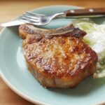 A juicy, pan-seared pork chop served with a side of creamy coleslaw on a light blue plate.