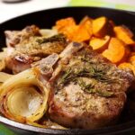 Close-up of juicy pork chops recipe served with roasted sweet potatoes and caramelized onions in a cast-iron skillet.