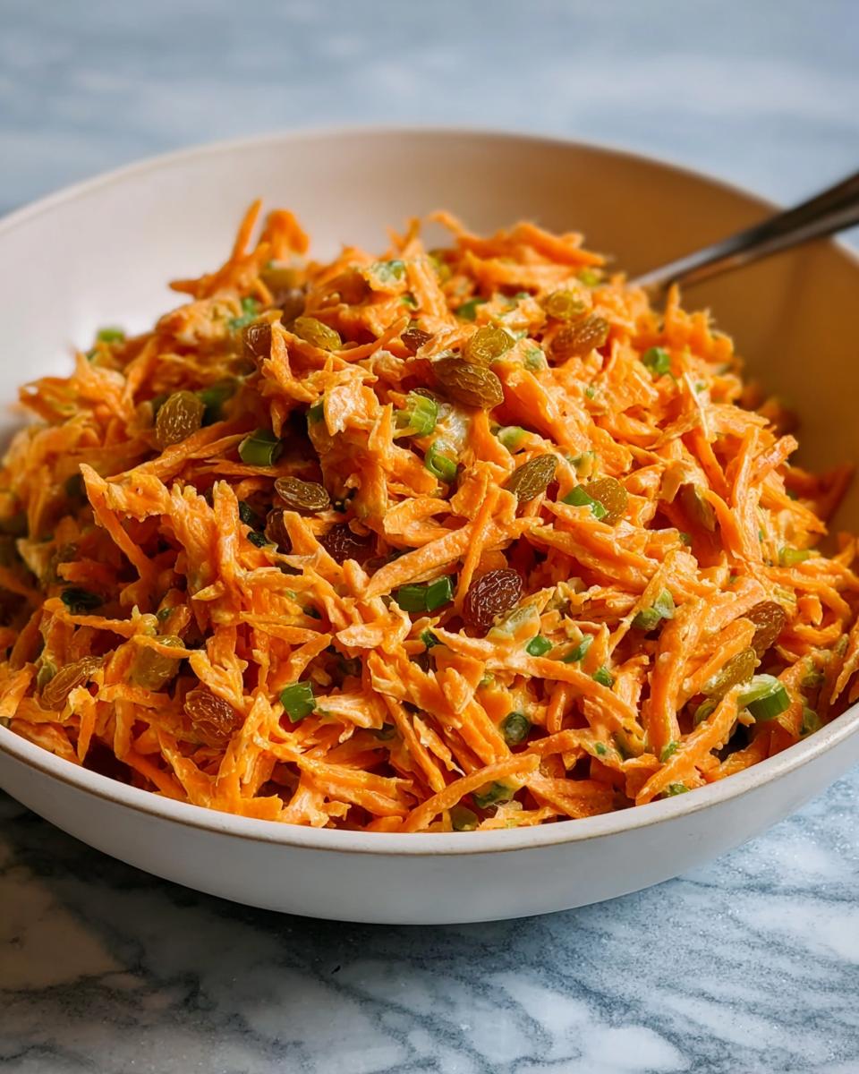 Close-up of a bowl filled with shredded carrots, raisins, and green onions, a quick veggie side.