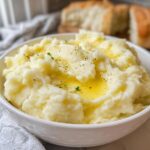 A bowl of fluffy mashed potatoes topped with melted butter, black pepper, and parsley, part of mashed potatoes recipes in 20 minutes.