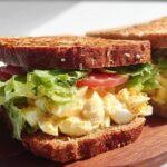 A delicious restaurant-style egg salad sandwich with whole wheat bread, lettuce, and tomato.
