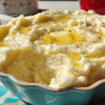 Close-up of creamy restaurant-style mashed potatoes with melted butter and black pepper.