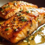 Two perfectly cooked salmon fillets with a golden-brown crust, drizzled in a garlic butter sauce and sprinkled with parsley. A restaurant-style salmon recipe.