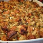 A close-up of a baking dish filled with golden-brown, fluffy restaurant-style stuffing, featuring cubes of bread, herbs, and vegetables.