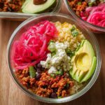 A vibrant and colorful rice bowl recipe for meal prep, featuring seasoned ground meat, black beans, rice, pickled red onions, feta cheese, and avocado.