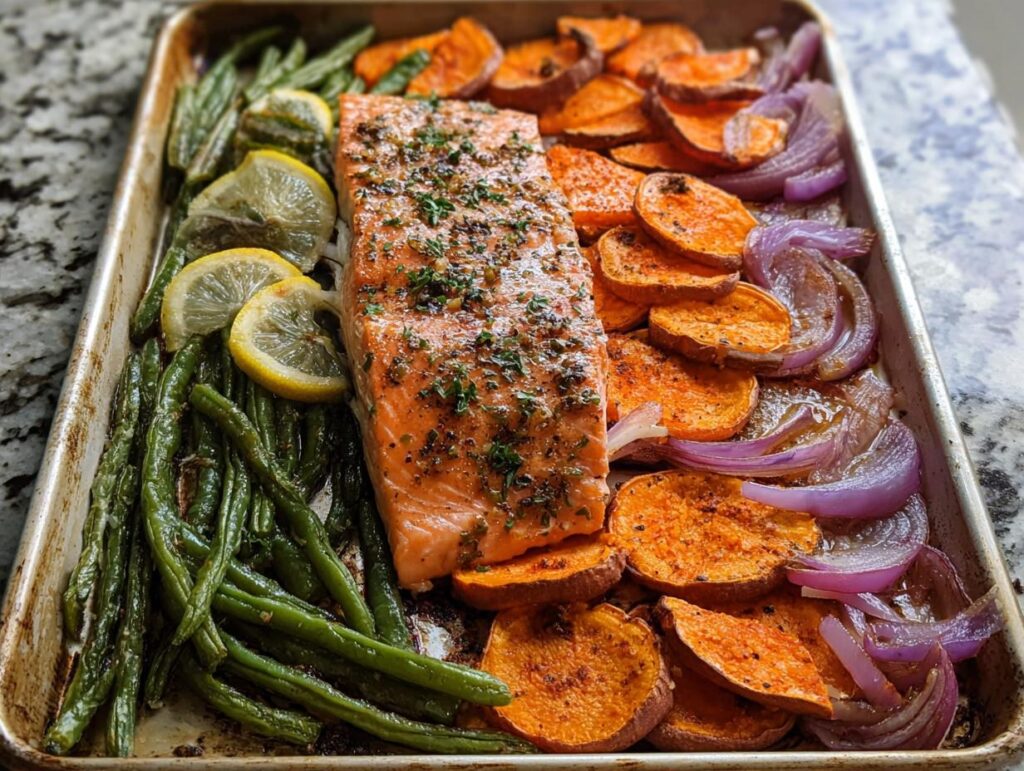 A delicious sheet pan meal prep featuring a salmon fillet with roasted sweet potatoes, green beans, red onions, and lemon slices.