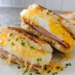 Two halves of a breakfast sandwich with fried egg, ham, melted cheese, and chives.
