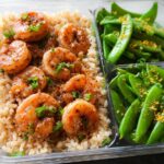 Meal prep container with seasoned shrimp over rice and a side of snap peas, perfect for shrimp recipes meal prep.