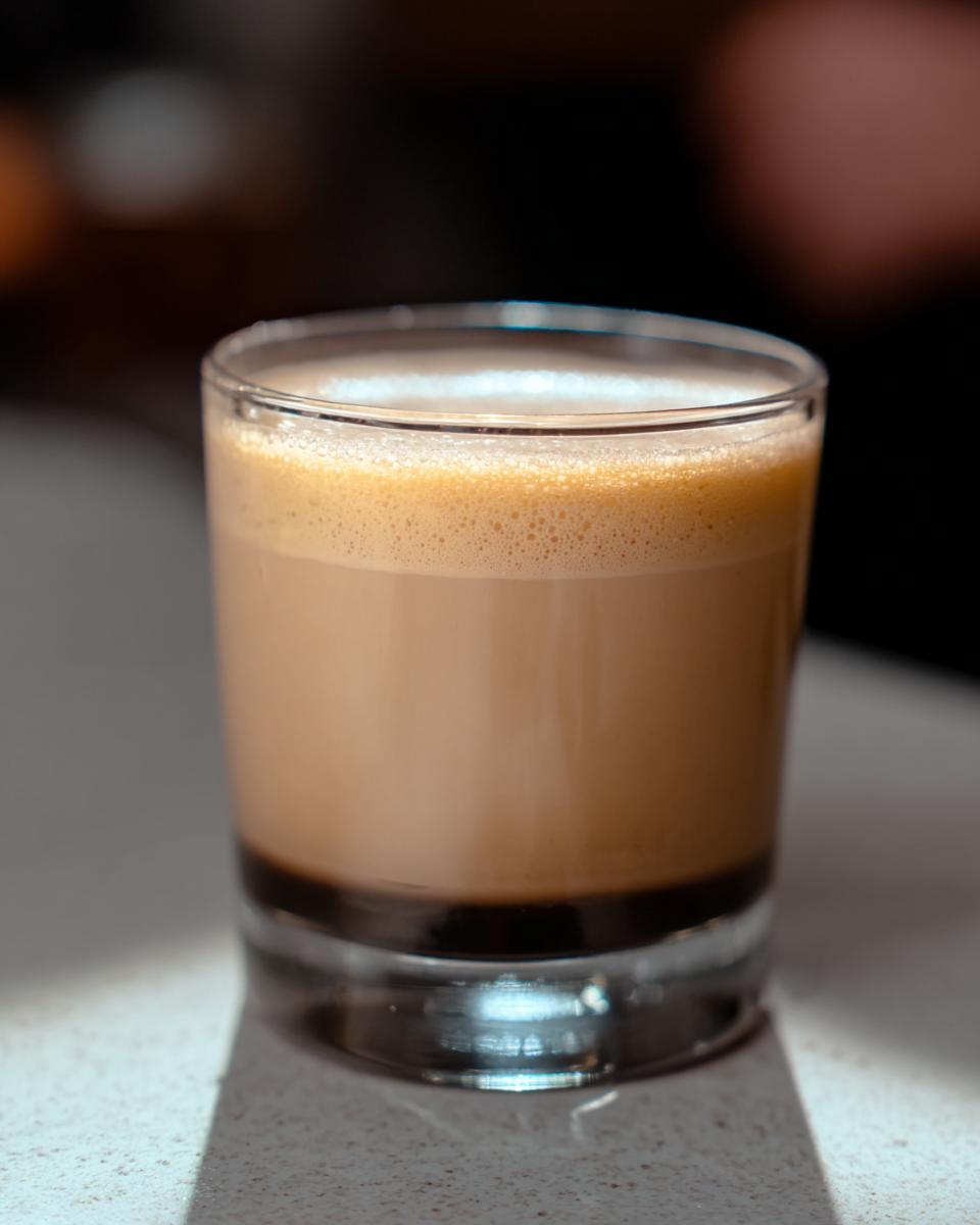 A close-up of a layered Starbucks drink with a foamy top in a glass, perfect for busy nights.