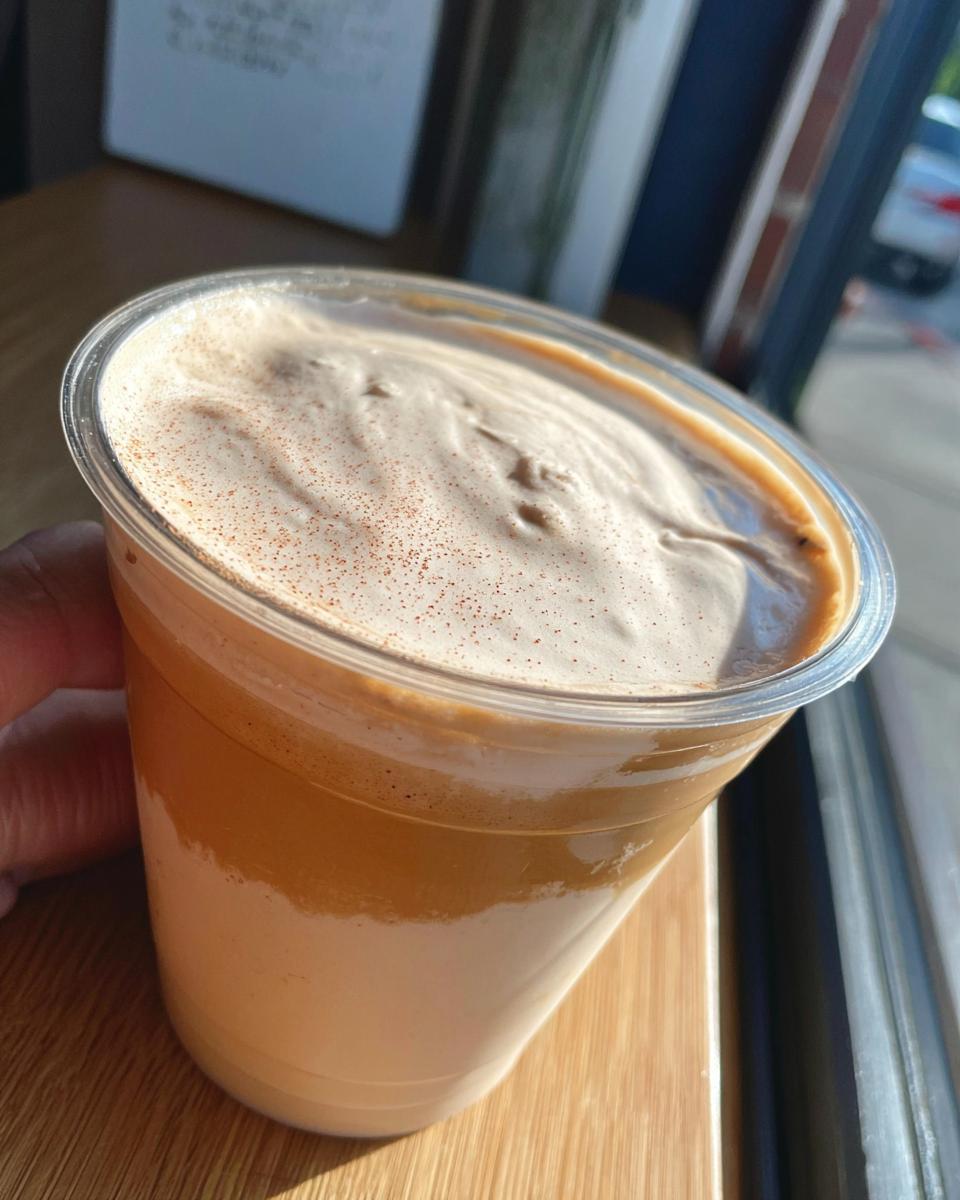A close-up of a frothy coffee drink in a clear plastic cup, sprinkled with cinnamon, perfect for Starbucks drinks recipes at home.