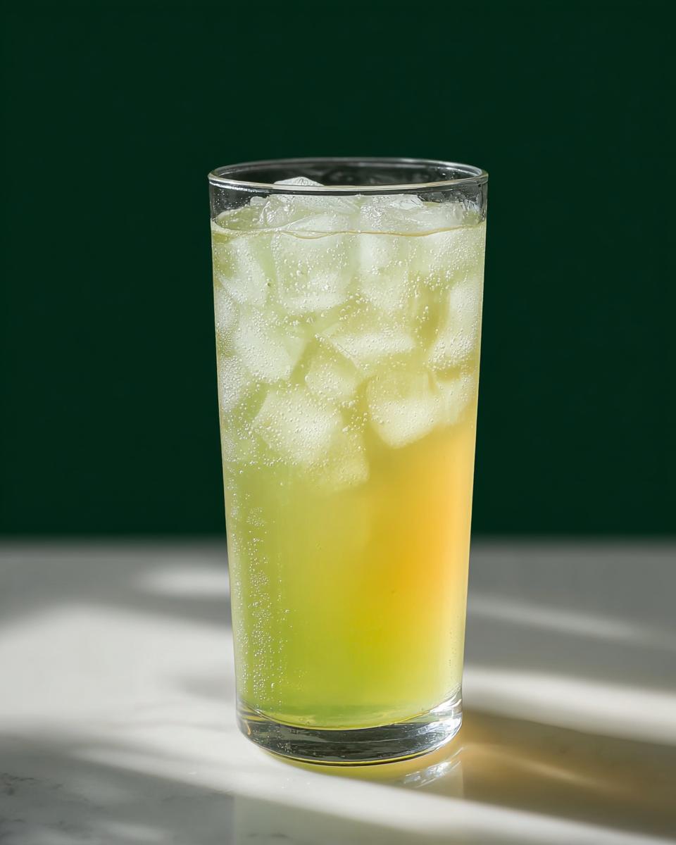 A tall glass filled with ice and a bubbly, layered green and yellow Starbucks drink.